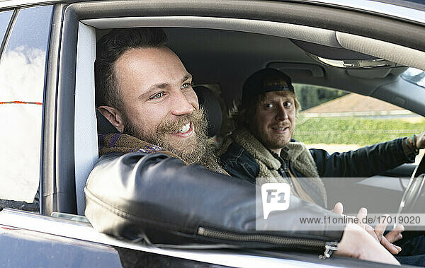 Man looking at smiling boyfriend while driving car seen through window