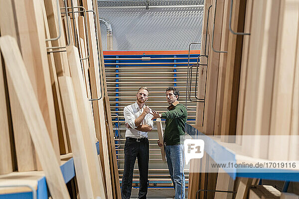 Zwei Zimmerleute unterhalten sich in einer Produktionshalle mit Holzbrettern im Vordergrund