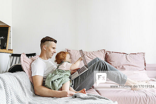 Mann mit kleiner Tochter arbeitet am Laptop auf dem Sofa