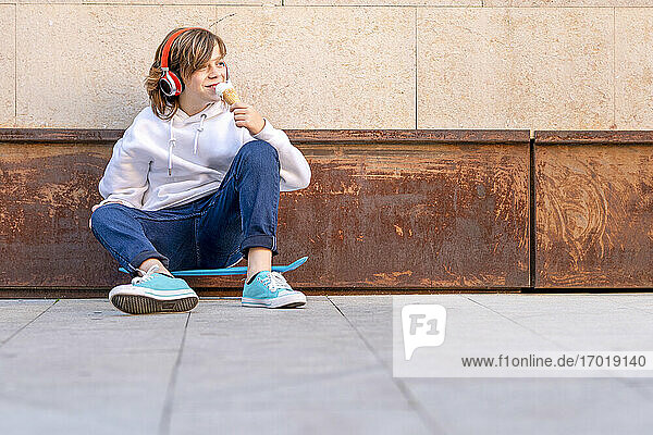 Junge mit Kopfhörern  der auf dem Gehweg sitzend ein Eis isst