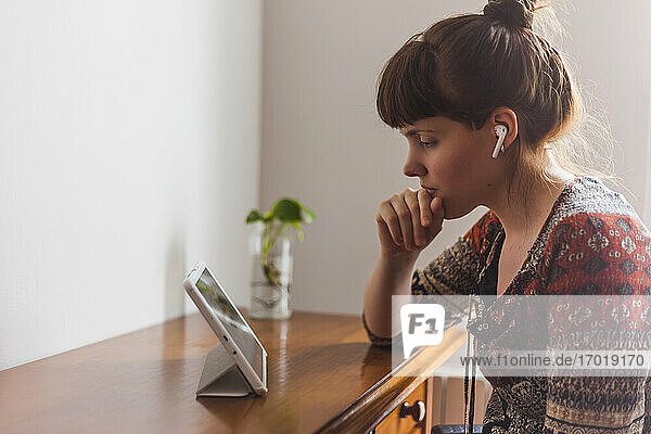 Junge Frau beim E-Learning über ein digitales Tablet mit drahtlosen Kopfhörern im heimischen Wohnzimmer