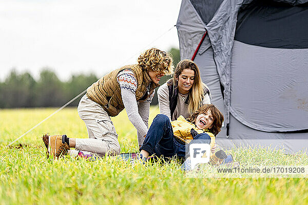 Three siblings playing on grass in front of pitched tent
