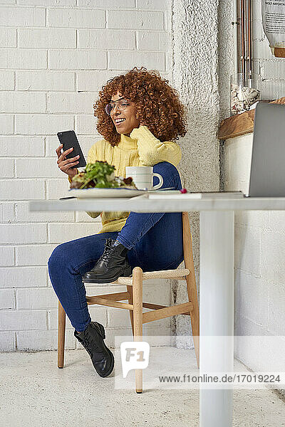 Glückliche Geschäftsfrau  die ein Smartphone benutzt  während sie auf einem Stuhl im Café sitzt