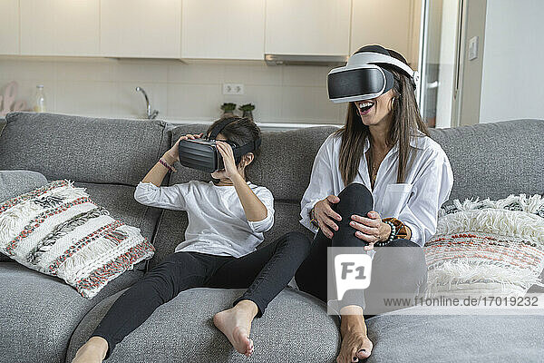 Mother and daughter using virtual reality glasses while sitting on sofa at home
