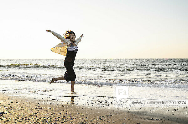 Unbeschwerte junge Frau läuft am Strand gegen den klaren Himmel bei Sonnenuntergang