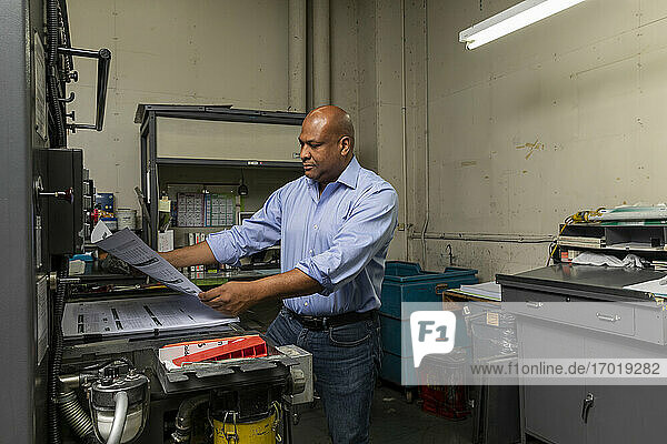 Männlicher Angestellter prüft Papier an einer Druckmaschine im Geschäft