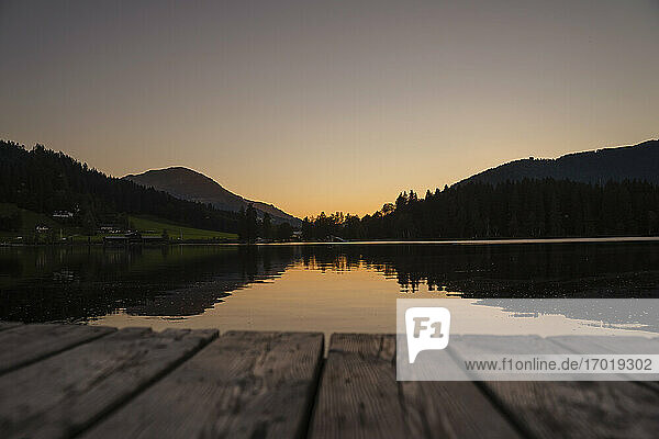 Mountains reflecting in shiny lake at dusk with edge of jetty in foreground