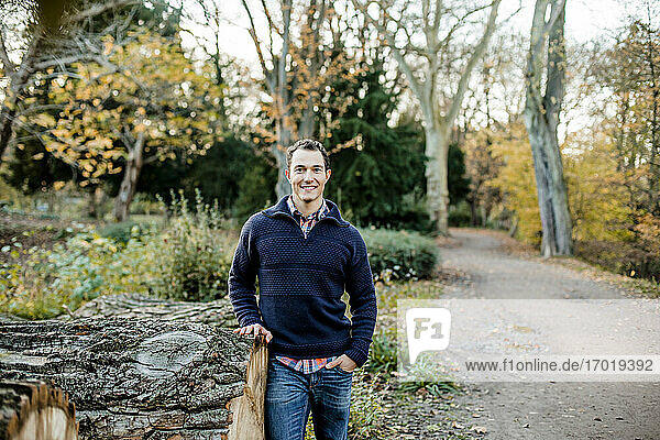Smiling handsome man with hand in pocket standing in front of trees at public park