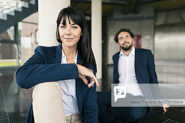 Confident businesswoman sitting by male colleague at office