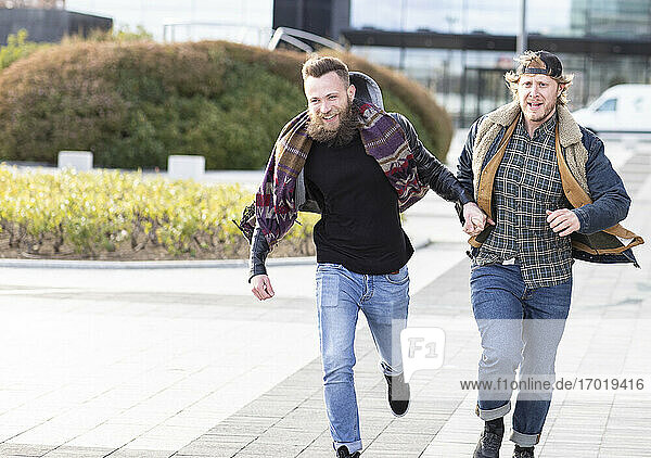 Gay boyfriends holding hands while running on street in city