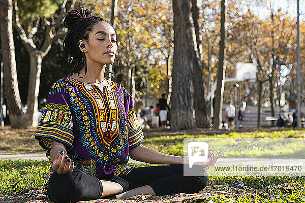Schöne junge Frau meditiert  während sie Yoga im Lotussitz im Park an einem sonnigen Tag praktiziert