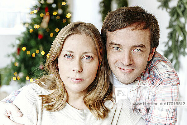 Nahaufnahme eines lächelnden Paares mit Weihnachtsbaum im Hintergrund zu Hause