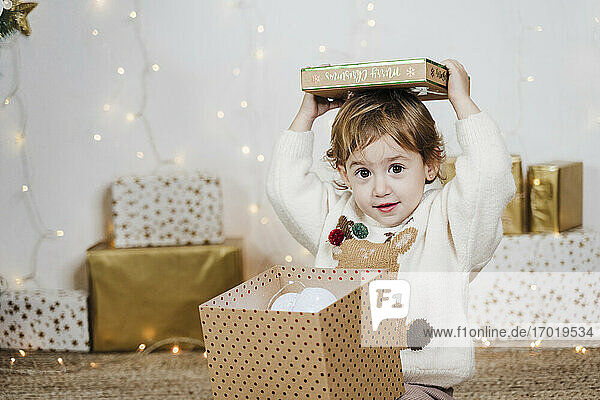 Niedliches kleines Mädchen  das zu Hause sitzend ein Weihnachtsgeschenk öffnet