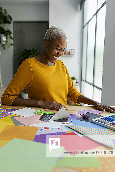 Lachende Origami-Künstlerin bei der Arbeit in ihrem Atelier mit buntem Papier