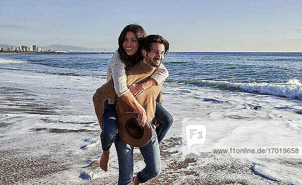Smiling boyfriend piggybacking girlfriend while walking at beach