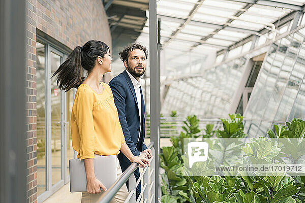 Männliche und weibliche Kollegen lehnen an einem Geländer im Büroflur