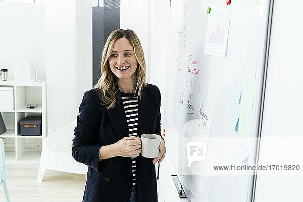 Smiling business woman standing at whiteboard in office