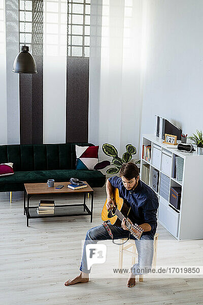 Männlicher Gitarrist  der im Studio sitzend auf der Gitarre probt