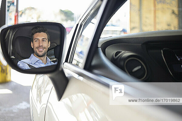 Spiegelbild eines lächelnden Geschäftsmannes beim Autofahren