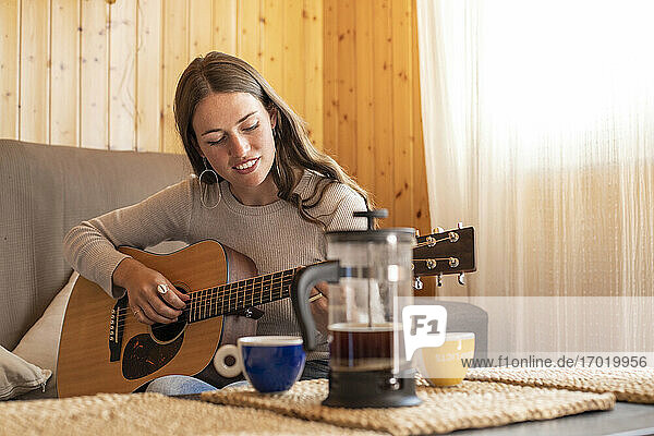 Junge Frau beim Üben mit Gitarre  während sie zu Hause auf dem Sofa sitzt