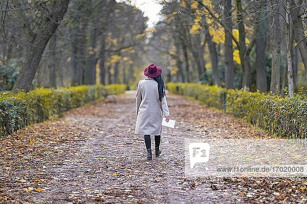 Mittlere erwachsene Frau mit Hut  die im Herbst auf einem Grundstück im Park spazieren geht