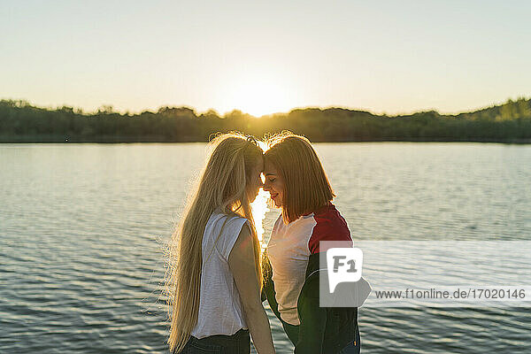 Lesbian couple standing face to face while standing against lake during sunset