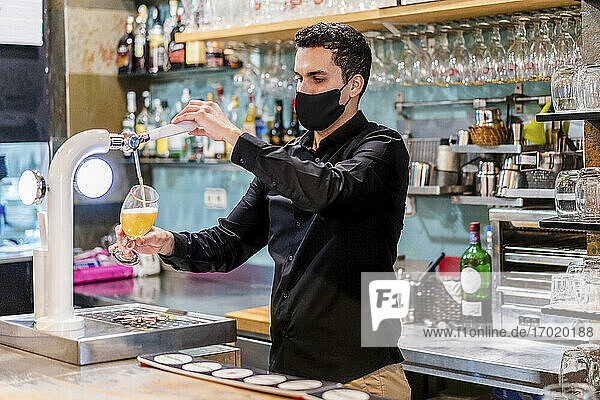 Portrait of bartender wearing protective face mask serving beer