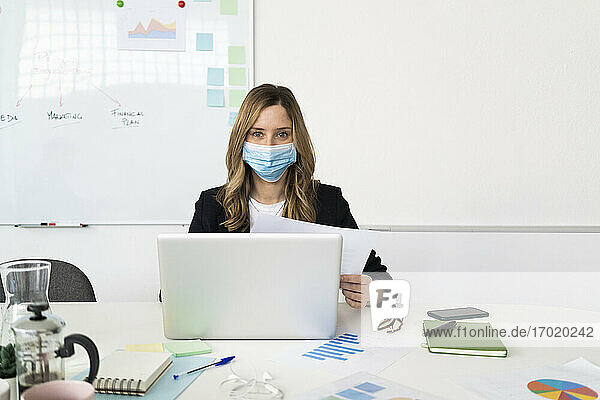 Woman wearing protective mask using laptop in office 