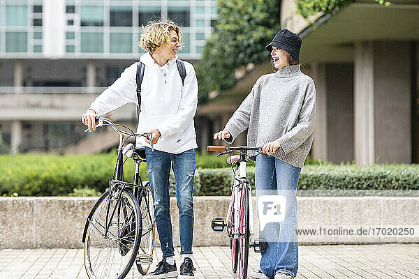 Cheerful friends standing with bicycle on footpath