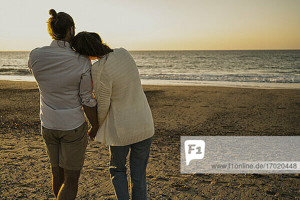 Romantisches Paar  das bei Sonnenuntergang am Strand spazieren geht