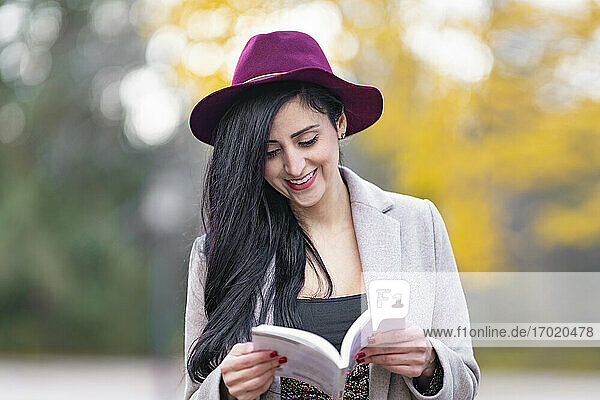 Lächelnde schöne Frau mit Hut  die am Wochenende im Park ein Buch liest