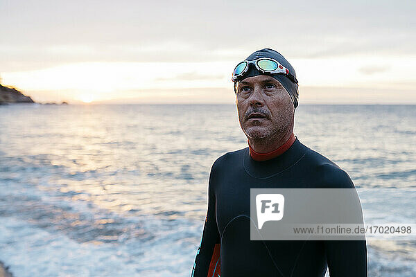Portrait of male swimmer standing alone on coastal beach at sunset