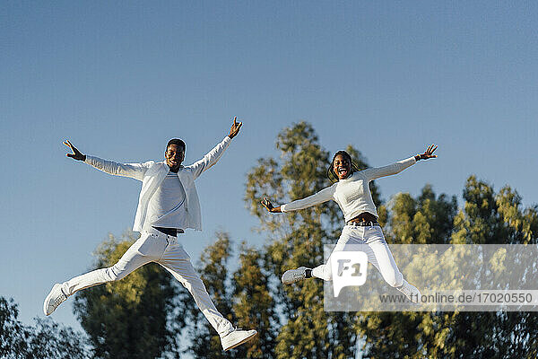 Fröhliches heterosexuelles Paar genießt den Tag beim Springen gegen den klaren Himmel im Sonnenlicht