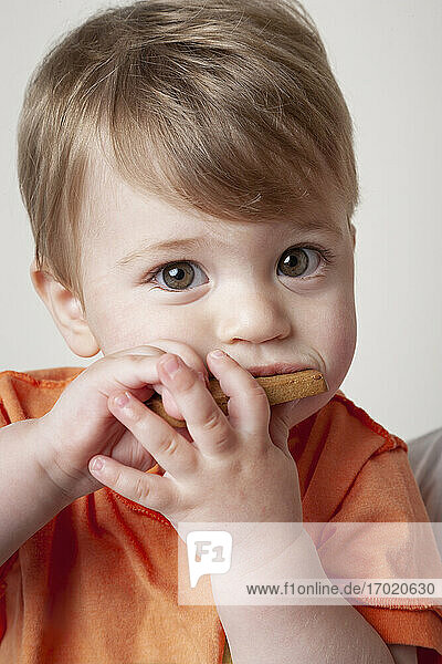 Kleiner Junge in orangefarbenem T-Shirt isst Keks
