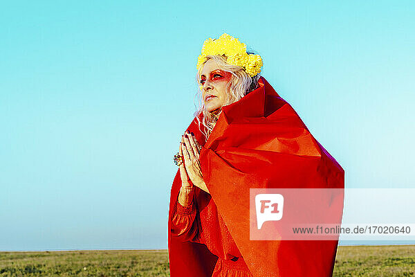 Senior woman with hands clasped against blue sky on sunny day