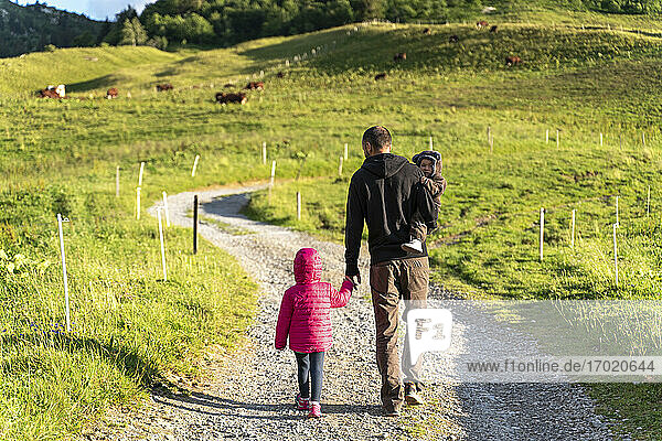 Vater geht mit zwei Kindern auf dem Wanderweg des Col des Aravis  Haute-Savoie an einem sonnigen Tag  Frankreich