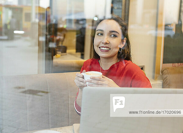 Lächelnde Frau mit Kaffeetasse durch Glas im Café gesehen