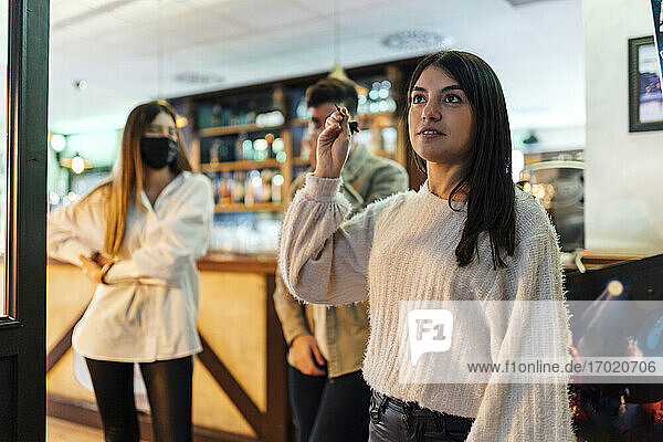 Junge Frau spielt Darts  während ihre Freunde in der Bar während der COVID-19 stehen