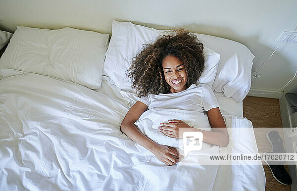 Fröhliche junge Frau liegt auf dem Bett und entspannt sich im Schlafzimmer zu Hause