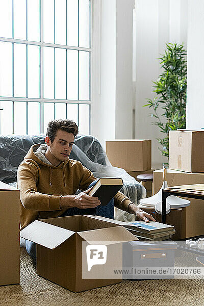 Young man unpacking books from box while moving in new loft apartment