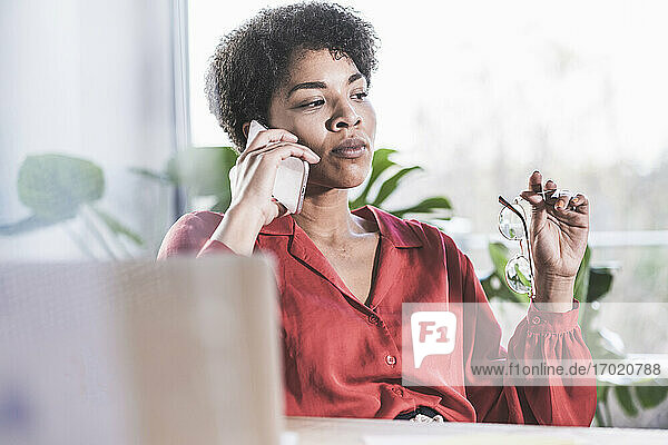 Frau  die zu Hause vor einem Laptop sitzt und mit einem Mobiltelefon spricht