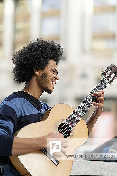 Junger Mann mit lockigem Haar  der im Freien stehend Gitarre spielt