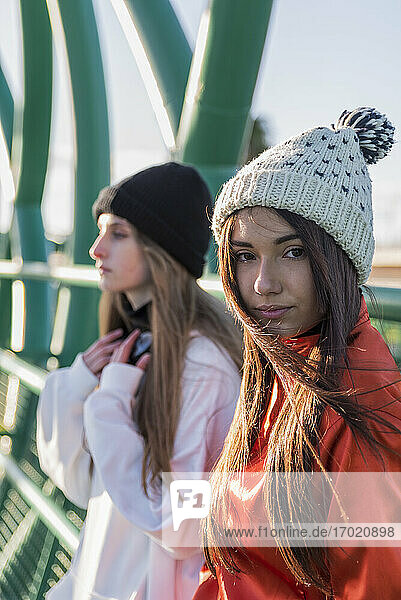 Junge Frau mit Strickmütze steht neben einem Freund auf einer Brücke
