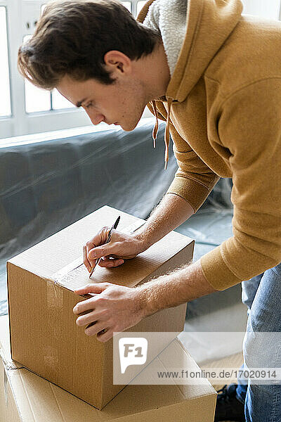 Junger Mann schreibt auf Karton beim Einzug in eine neue Loftwohnung