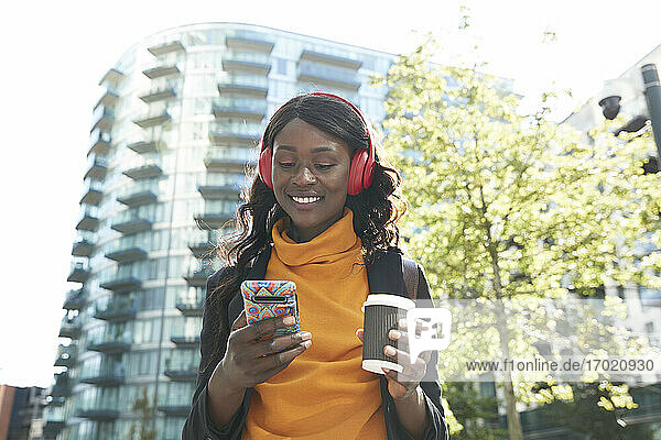 Lächelnde weibliche Fachkraft mit Einweg-Kaffeebecher hört Musik im Büropark