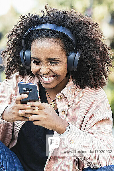 Fröhliche junge Frau hört Musik und benutzt ein Mobiltelefon in der Stadt