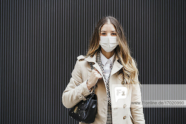 Mittlere erwachsene Frau mit Handtasche und Gesichtsschutzmaske vor schwarzer Wand