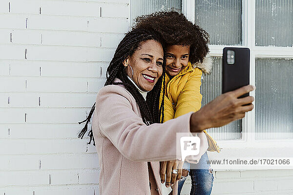 Lächelnde Mutter nimmt Selfie mit Tochter gegen die Wand