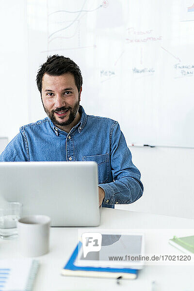 Porträt eines lächelnden Mannes mit Laptop im Büro