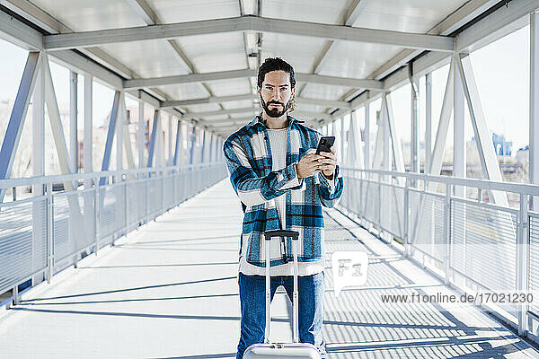 Mann mit Handy und Gepäck  der auf einer Brücke steht